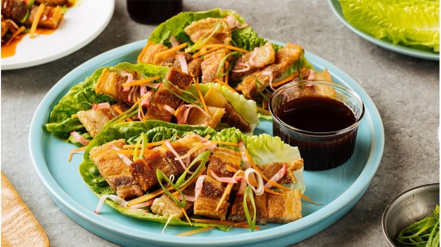 Crispy Lechon Kawali wrapped in lettuce and served with sauce on a sea foam blue plate. Crispy Lechon Kawali wrapped in lettuce and served with sauce on a sea foam blue plate.