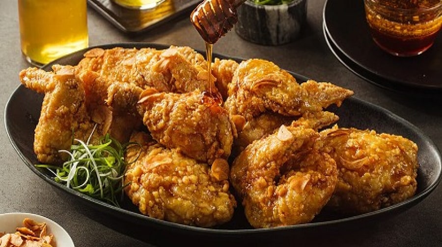 Flat lay of crispy fried chicken on a black plate with drizzles of honey sauce Flat lay of crispy fried chicken on a black plate with drizzles of honey sauce