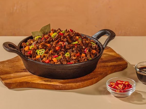 Bopis in a cast-iron pan over a wooden board. 