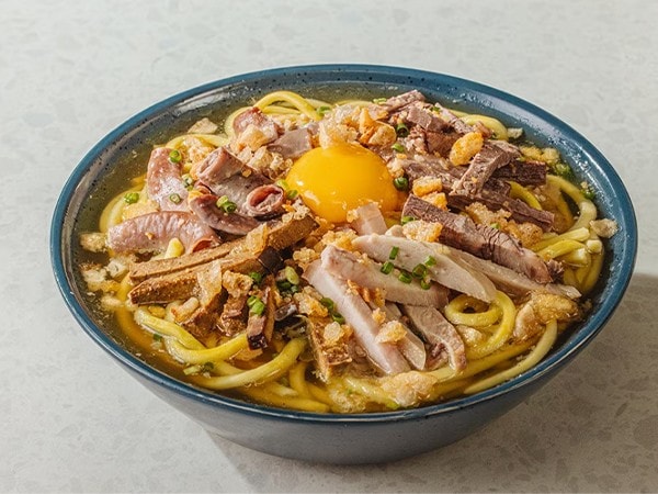 La Paz batchoy with fresh egg in a dark bowl. 