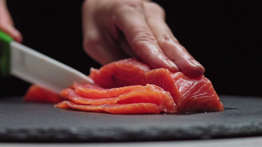 Fresh orange salmon being sliced very thinly with a sharp knife Fresh orange salmon being sliced very thinly with a sharp knife