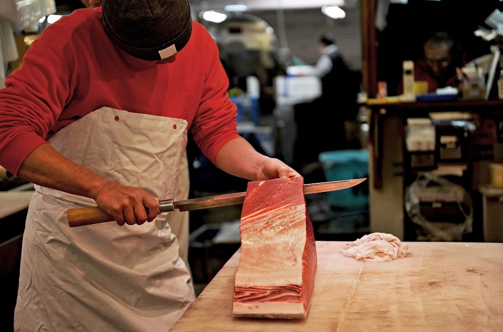 A fishmonger skillfully filleting a tuna with a long blade A fishmonger skillfully filleting a tuna with a long blade