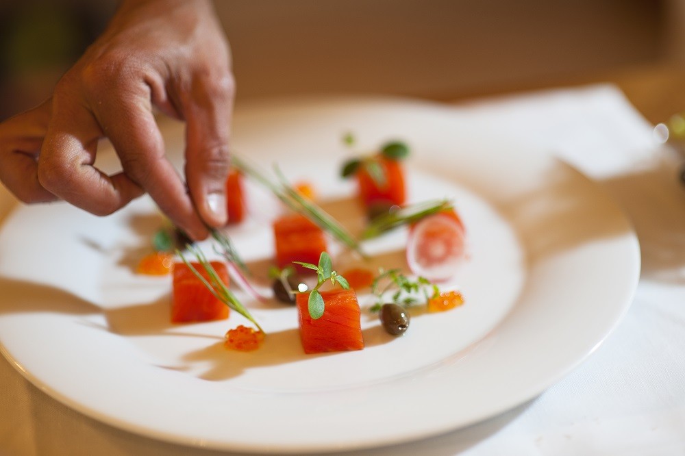 A chef plating up a salmon sashimi dish with garnishes A chef plating up a salmon sashimi dish with garnishes