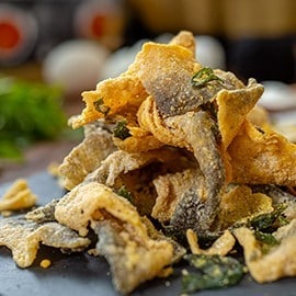 Crispy fish skin coated with salted egg powder on a black tray. Crispy fish skin coated with salted egg powder on a black tray.