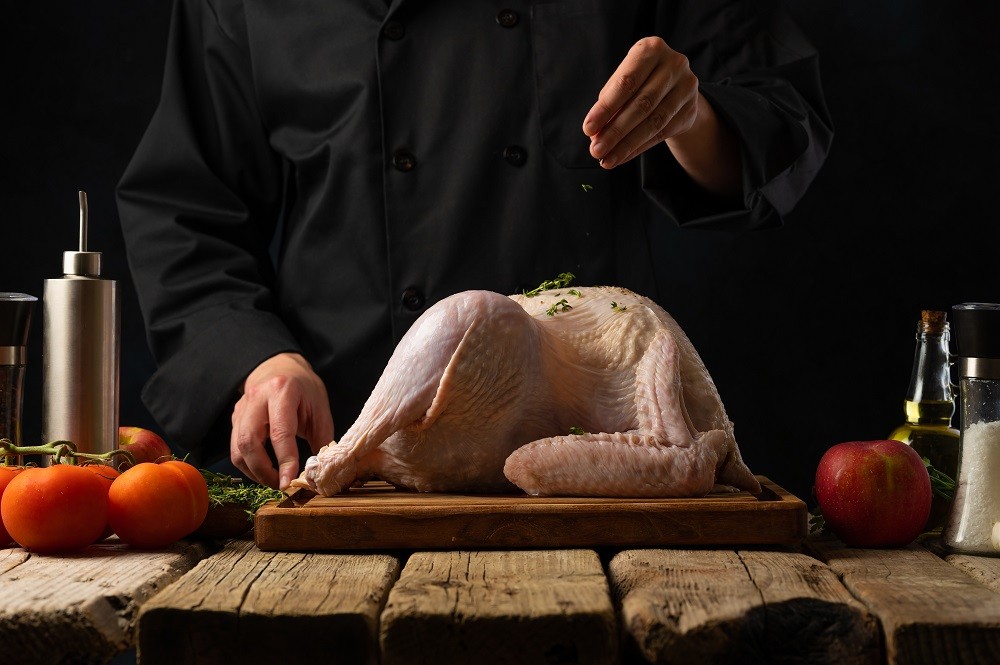 A professional chef is seasoning a whole turkey on a wooden chopping board A professional chef is seasoning a whole turkey on a wooden chopping board