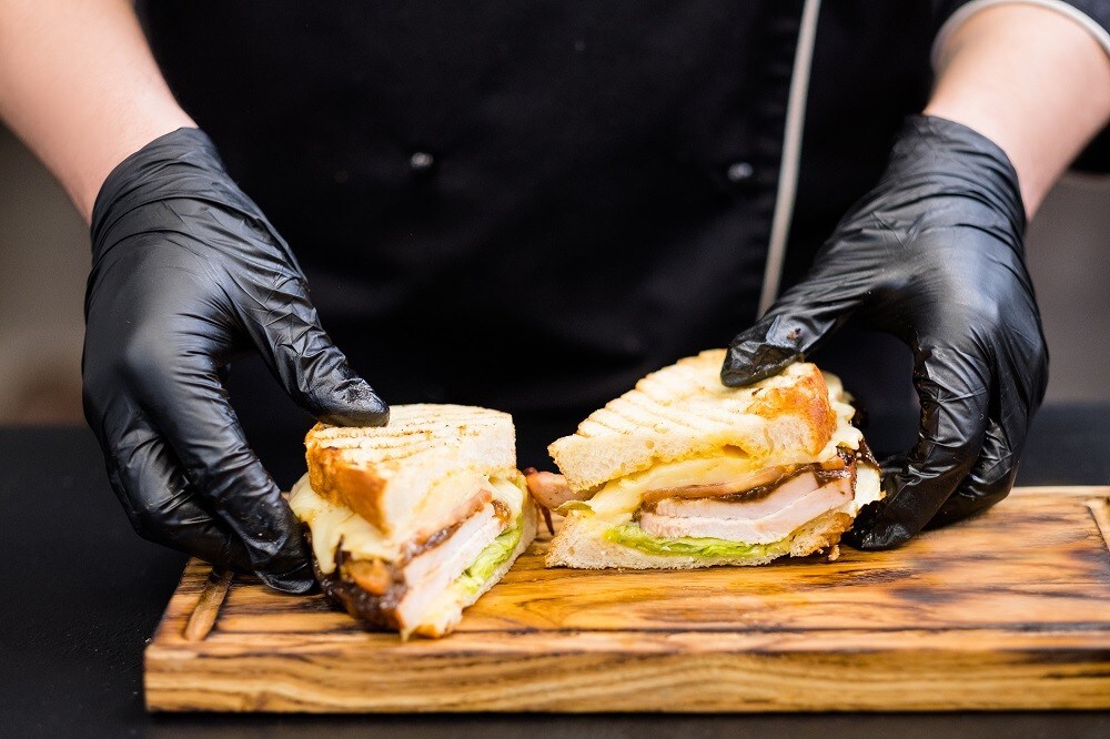 A closeup photo of chef serving half-cut grilled turkey breast sandwich A closeup photo of chef serving half-cut grilled turkey breast sandwich