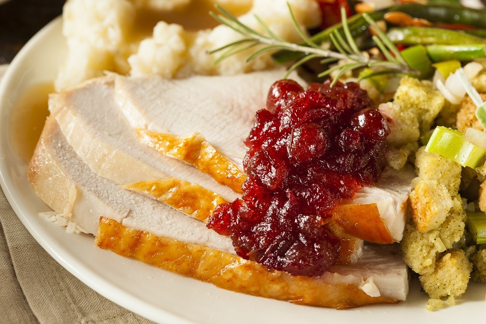 A plate stacked with roast turkey slices, cranberry sauce, stuffing, mashed potato, and greens A plate stacked with roast turkey slices, cranberry sauce, stuffing, mashed potato, and greens
