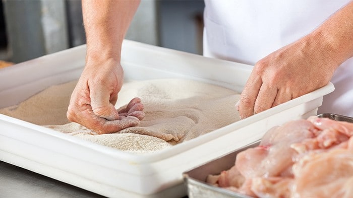 Chicken pieces being dredged in a container with flour and starch. 