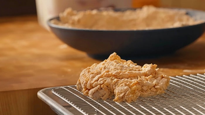 A piece of raw, bread chicken on a wire rack before frying.