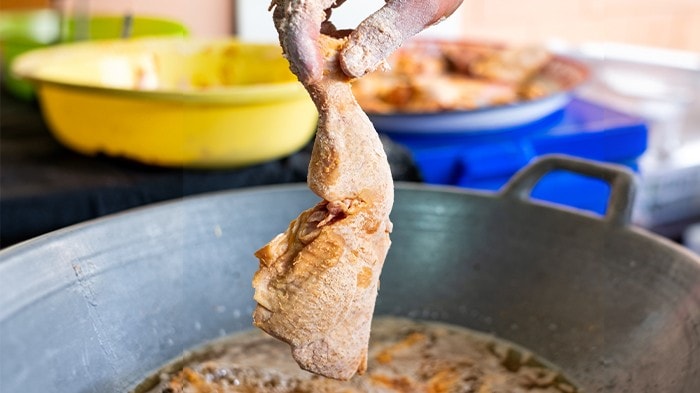 Hand holding a piece of breaded quarter chicken before frying. 