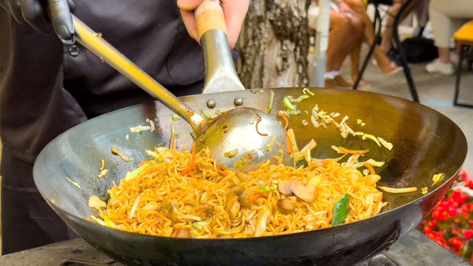 Chef stir-frying noodles in a wok.