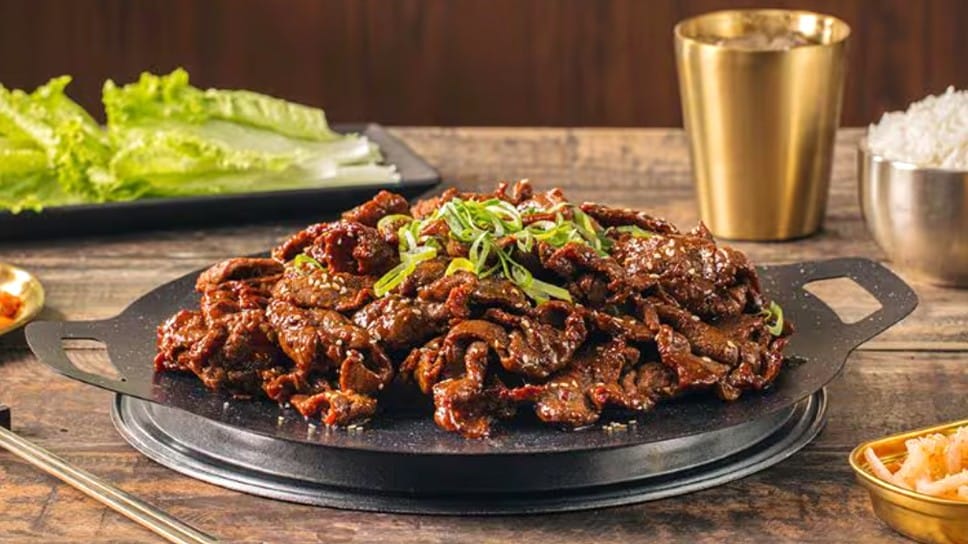 Beef bulgogi on a pan surrounded by kimchi, lettuce, and rice. 