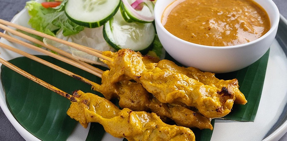 A plate of chicken satay with peanut sauce on the side.