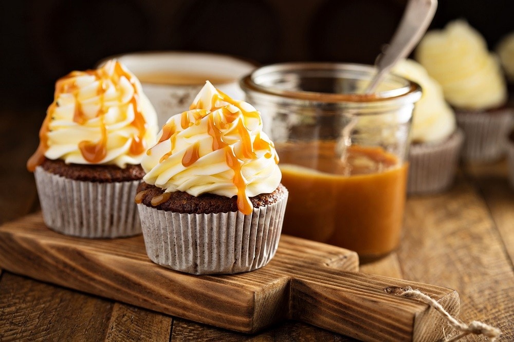 Two butterscotch cupcakes with white cream and caramel sauce drizzles Two butterscotch cupcakes with white cream and caramel sauce drizzles