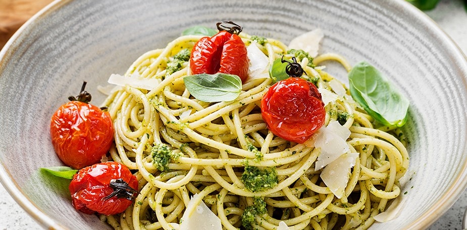 Pesto spaghetti with basil leaves, Parmesan, and cherry tomatoes. 