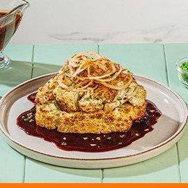 Cauliflower bistek on a gray plate with sauce on the side.