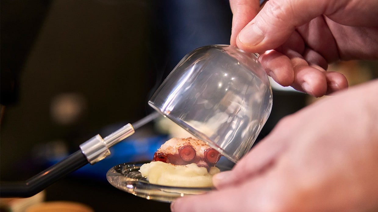 A chef using a smoke gun infuse a pulpo dish with woody aroma. A chef using a smoke gun infuse a pulpo dish with woody aroma.
