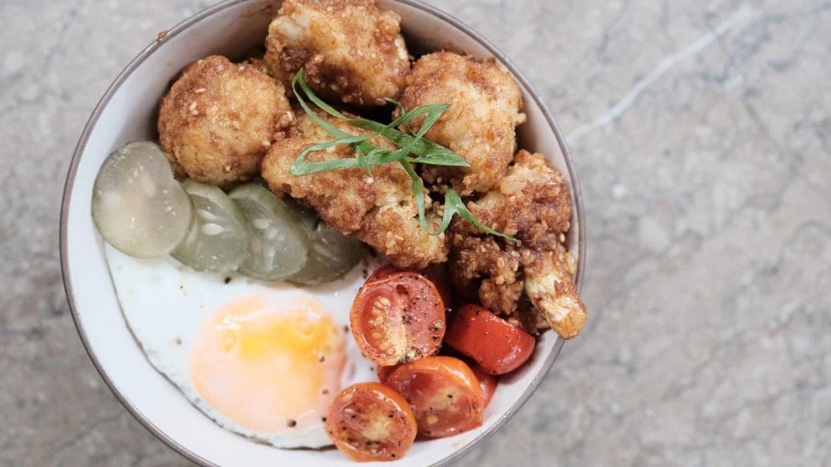 A rice bowl topped with fried chicken cutlets, a fried egg, tomatoes, and pickles A rice bowl topped with fried chicken cutlets, a fried egg, tomatoes, and pickles