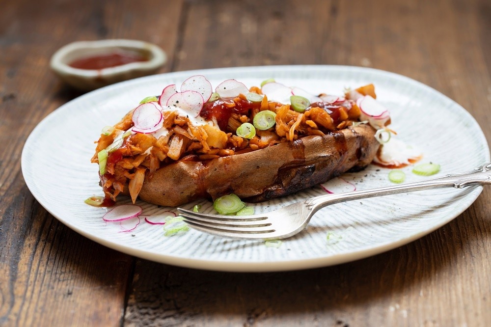 A plate of baked potato filled with barbecued jackfruit A plate of baked potato filled with barbecued jackfruit