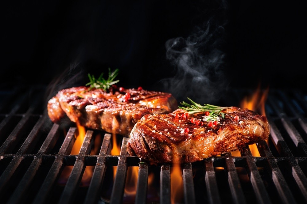 Beef steaks and fresh herb on a grill with flame Beef steaks and fresh herb on a grill with flame