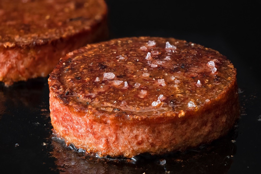 A plant-based burger patty being cooked on flat back iron grill A plant-based burger patty being cooked on flat back iron grill