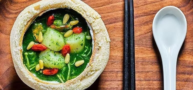 A bowl of green vegetable soup with potatoes in a bread bowl. A bowl of green vegetable soup with potatoes in a bread bowl.