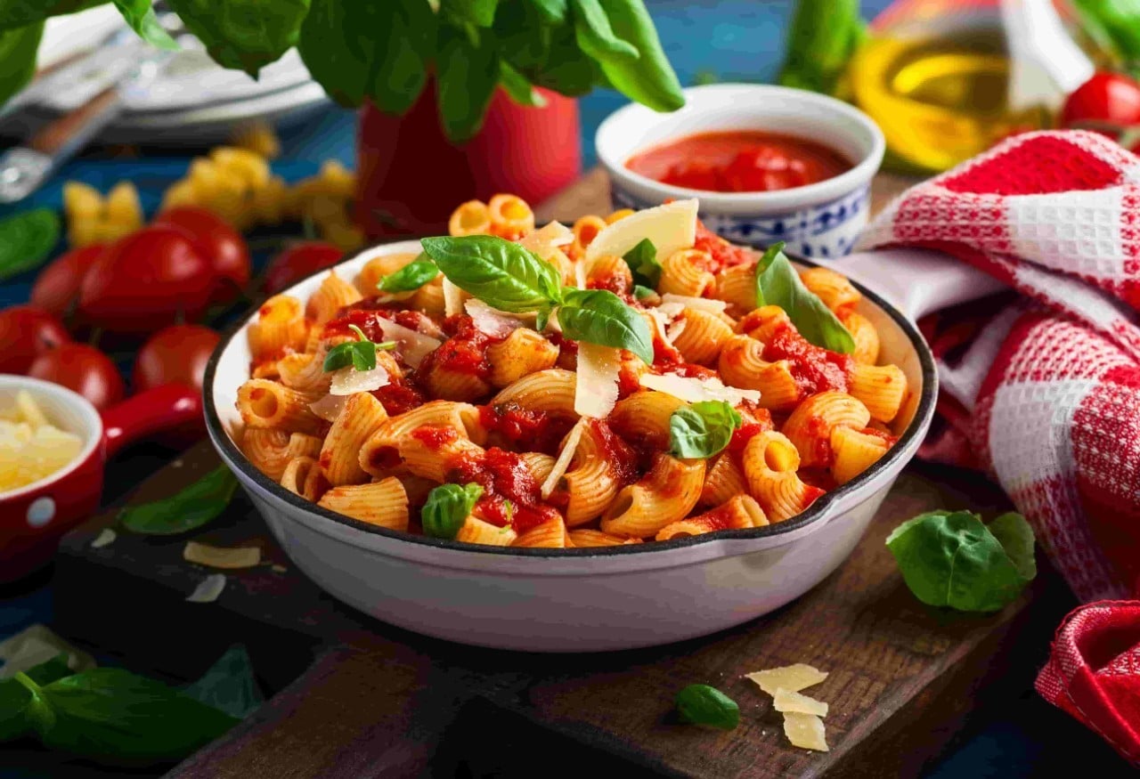 A bowl of tomato and macaroni pasta garnished with basil. A bowl of tomato and macaroni pasta garnished with basil.