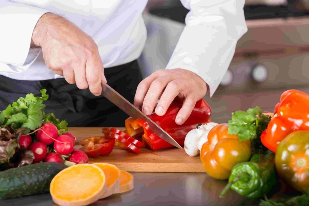 A chef cutting fresh vegetables on a wooden board, including red bell peppers. A chef cutting fresh vegetables on a wooden board, including red bell peppers.