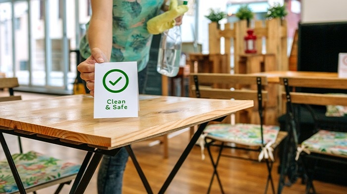 A restaurant staff placing a “Clean & Safe” sign on a table.