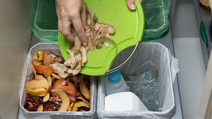 A person placing food scraps in its proper waste segregation bin.