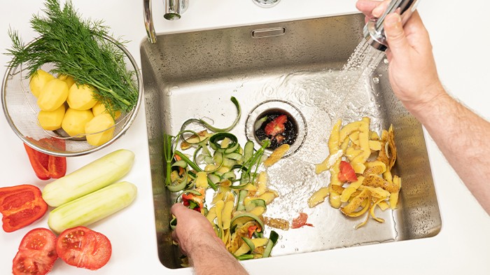 Kitchen scraps and vegetable peels being rinsed in a sink.