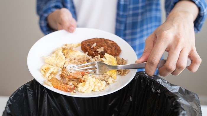 Person scraping leftover food from plate into garbage bin.
