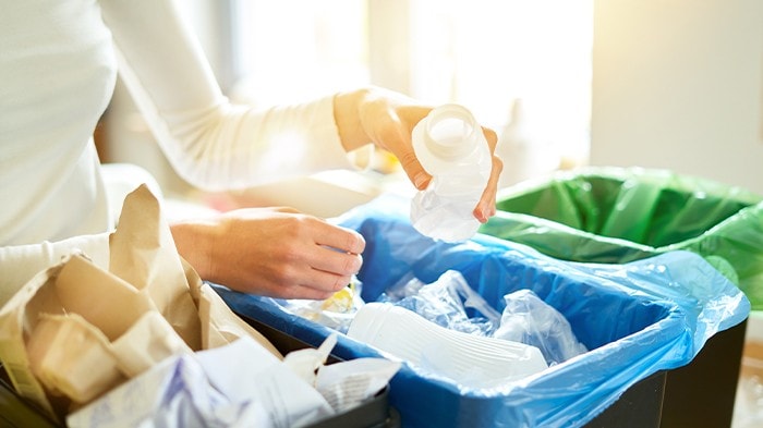 Woman placing plastic bottle in recycling bin at home.