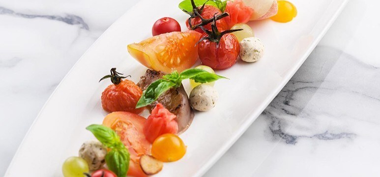 An appetizer of tomatoes, cheese, and basil leaves on a white platter. An appetizer of tomatoes, cheese, and basil leaves on a white platter.