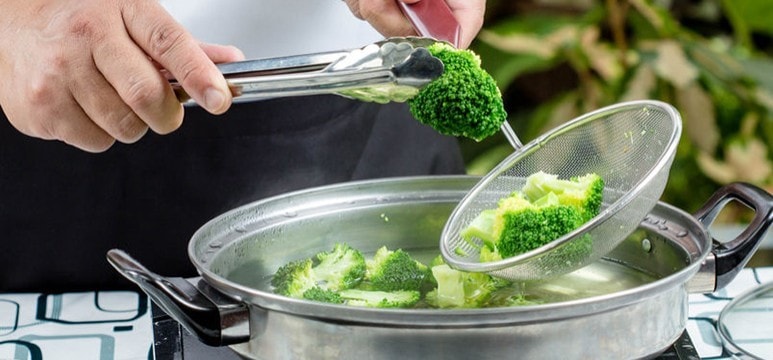 A cook boiling broccoli florets in a pot. A cook boiling broccoli florets in a pot.