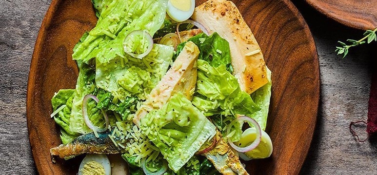 A plate of Caesar salad with lettuce, onions, egg, and chicken strips. A plate of Caesar salad with lettuce, onions, egg, and chicken strips.