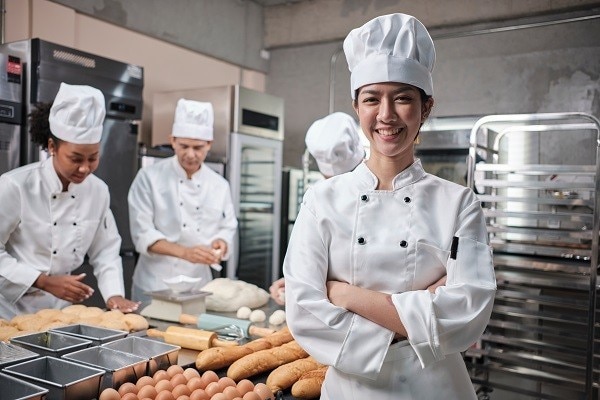 A happy female cook in front of other cooks making bread