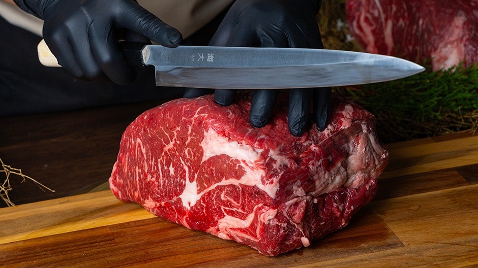 A chef slicing a large cut of beef placed on a wooden chopping board.