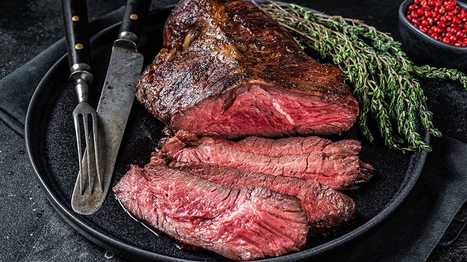 Grilled hanger steak with some slices on a black plate.