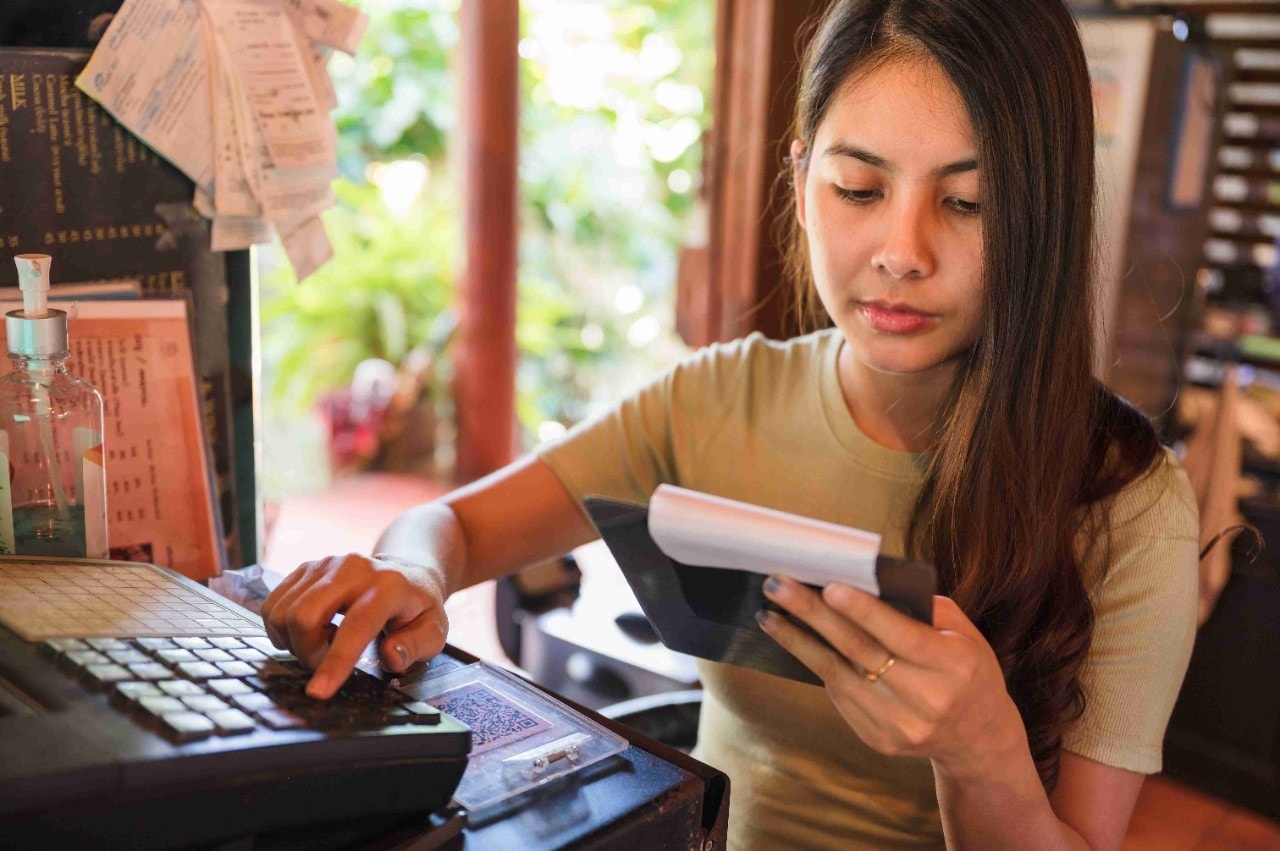 A restaurant owner checking order bills and using the point of sale system to adjust prices due to food inflation A restaurant owner checking order bills and using the point of sale system to adjust prices due to food inflation