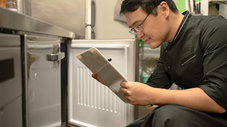A chef checking the contents of an undercounter refrigerator. 