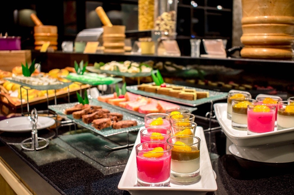 A buffet area showcasing little servings of pink gelatine, mousse, and mini cakes on serving plates A buffet area showcasing little servings of pink gelatine, mousse, and mini cakes on serving plates