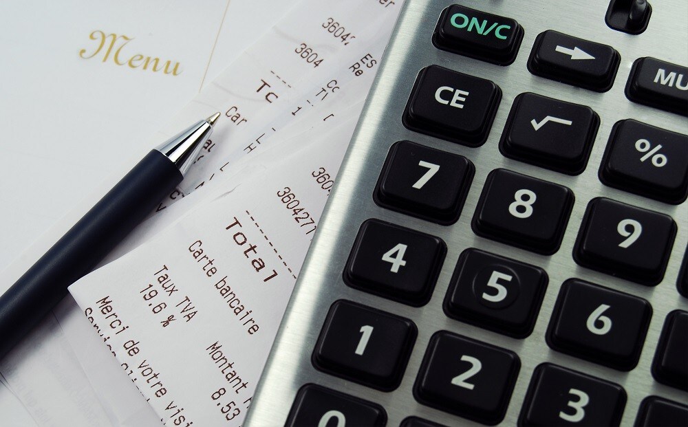 A tight shot of a silver calculator with a white restaurant menu, official receipts, and ballpen A tight shot of a silver calculator with a white restaurant menu, official receipts, and ballpen