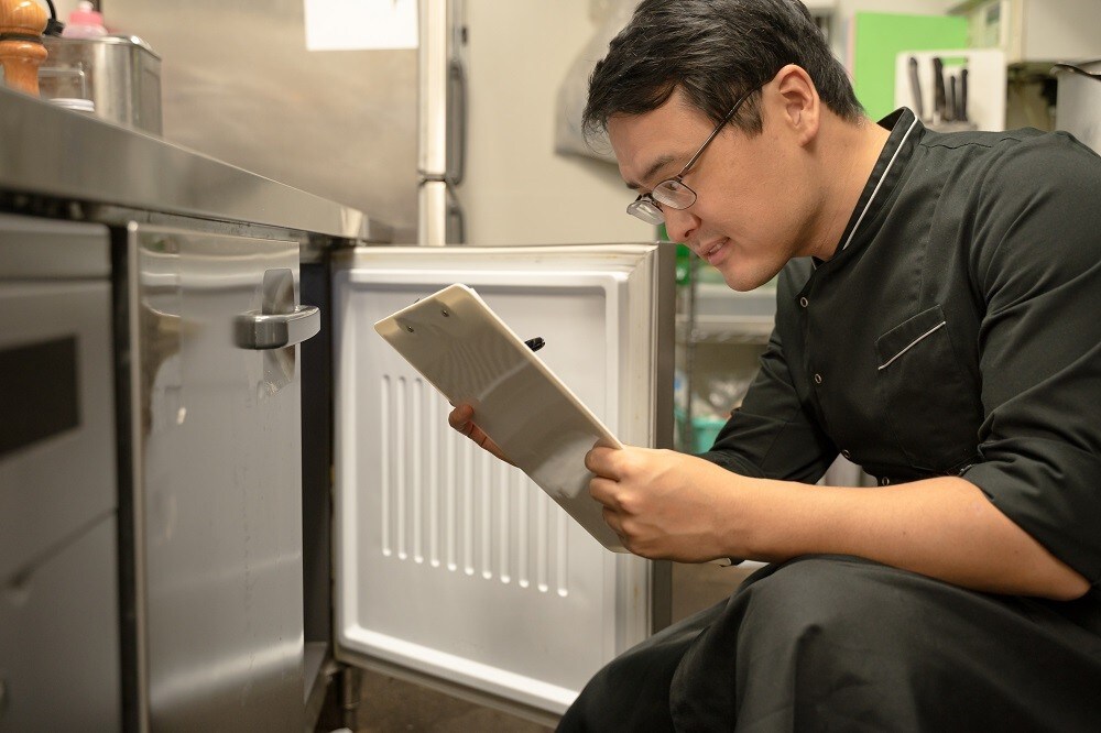 A male kitchen staff checks inventory of ingredients inside a chiller A male kitchen staff checks inventory of ingredients inside a chiller