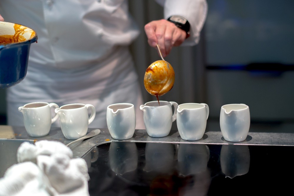 A chef scoops sauce from a pot into white sauce boats A chef scoops sauce from a pot into white sauce boats