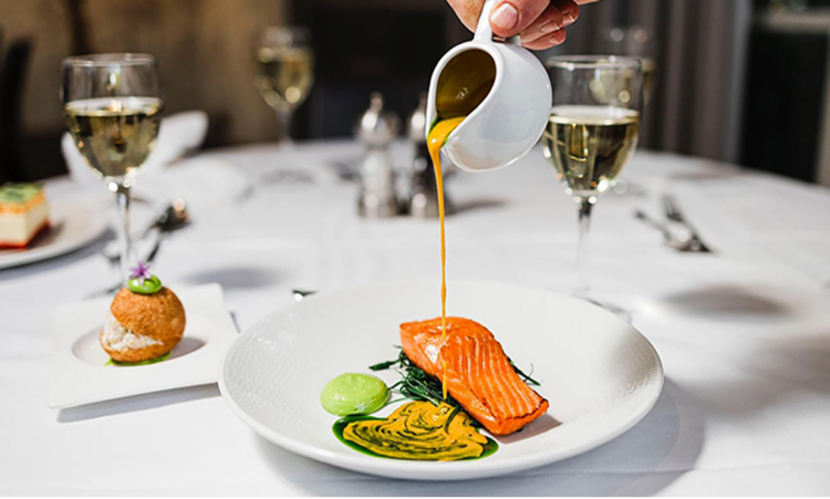A server pours sauce over a salmon dish. 