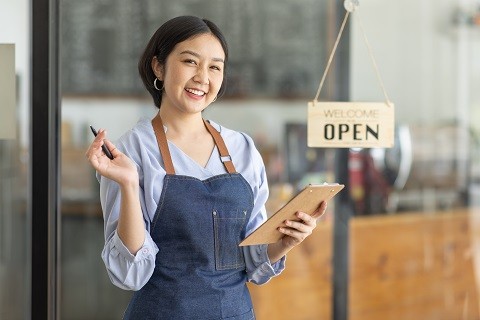 A restaurant server holding a clipboard beside an open sign. A restaurant server holding a clipboard beside an open sign.