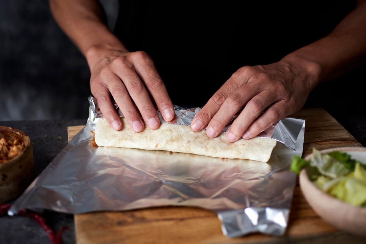 A man rolling a salad wrap in aluminum foil. A man rolling a salad wrap in aluminum foil.