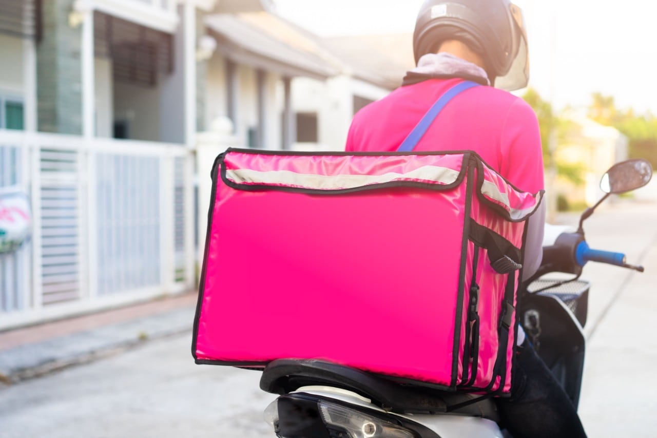 A delivery man wearing a pink uniform on a motorbike. A delivery man wearing a pink uniform on a motorbike.