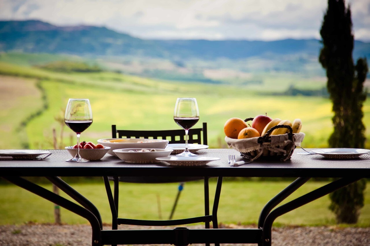 A table with glasses of wine and a fruit basket overlooking a landscape. A table with glasses of wine and a fruit basket overlooking a landscape.